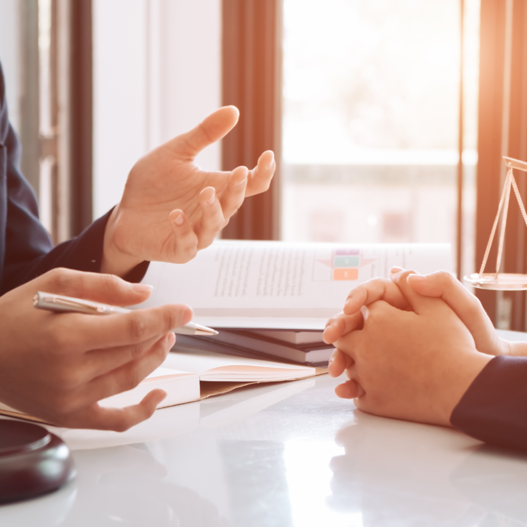 Two professionals in a one-on-one coaching conversation at a desk with a notebook and pen, warm window light in a modern office.