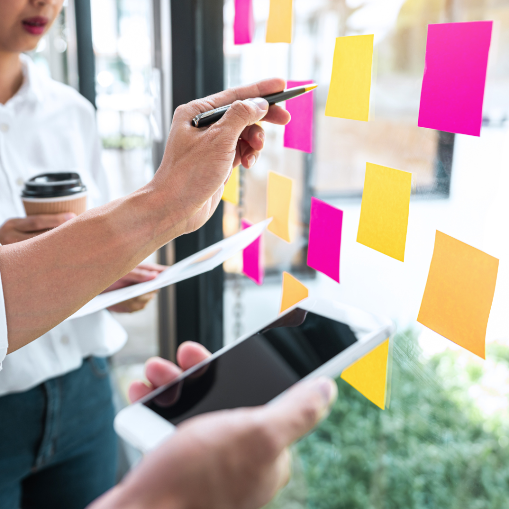 Facilitator pointing to colorful sticky notes on a glass wall during a team sales training workshop.